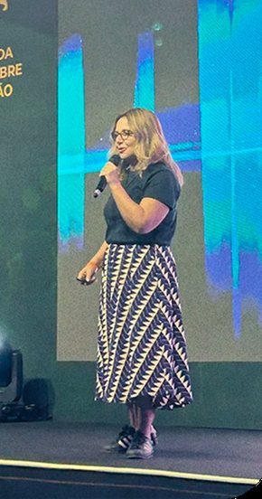 Claudia Fernandes palestrando em palco com telão